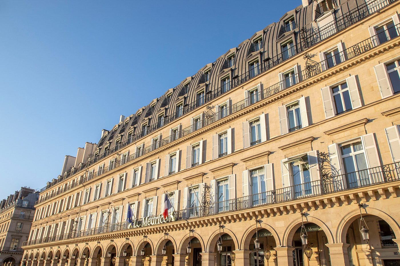 La longue façade du Meurice sous les arcades de la rue de Rivoli, drapeaux au-dessus de l'entrée