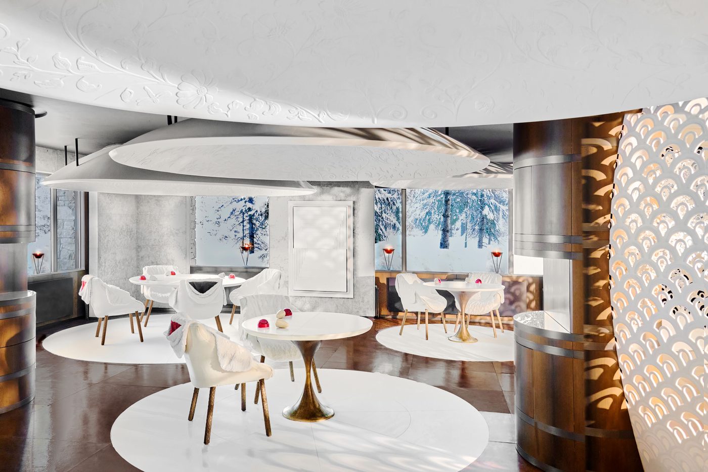 La salle blanche du 1947 à Cheval Blanc, tables rondes et fauteuils clairs sous un plafond sculpté, sapins enneigés derrière les vitres