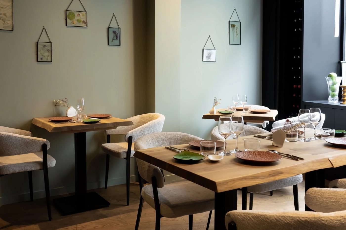 La salle d'Aldéhyde : murs vert d'eau, tables en bois brut, chaises beiges et cadres de plantes séchées