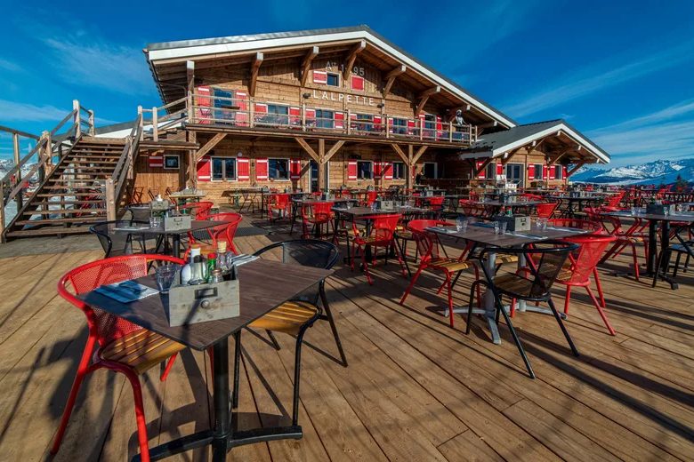 La terrasse en bois de L'Alpette, chaises rouges et tables au soleil devant le chalet, ciel bleu