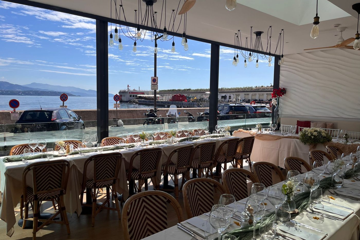 La salle d'Amici Miei, longue table dressée devant les baies vitrées ouvertes sur le port de Fontvieille