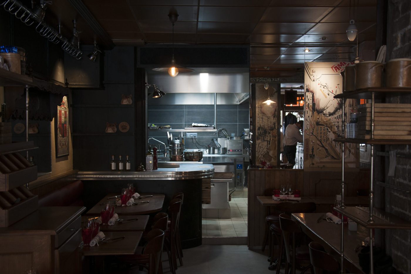 La salle étroite de L'Ami Jean, tables dressées, menant à la cuisine ouverte carrelée de gris