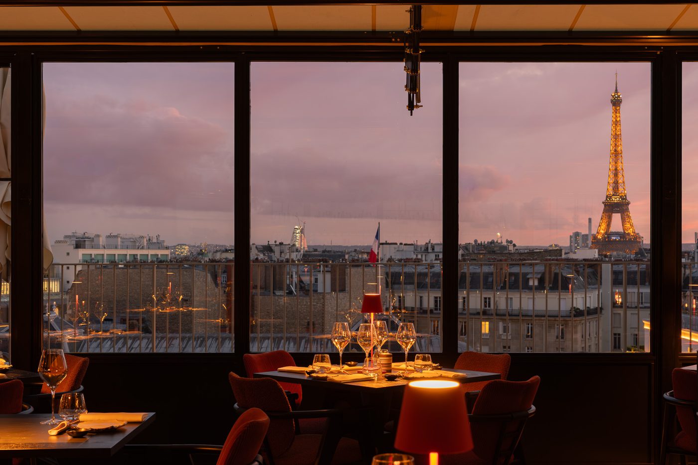 La terrasse d'hiver d'Aqua Kyoto derrière ses baies vitrées, tables dressées et lampes rouges, la tour Eiffel illuminée