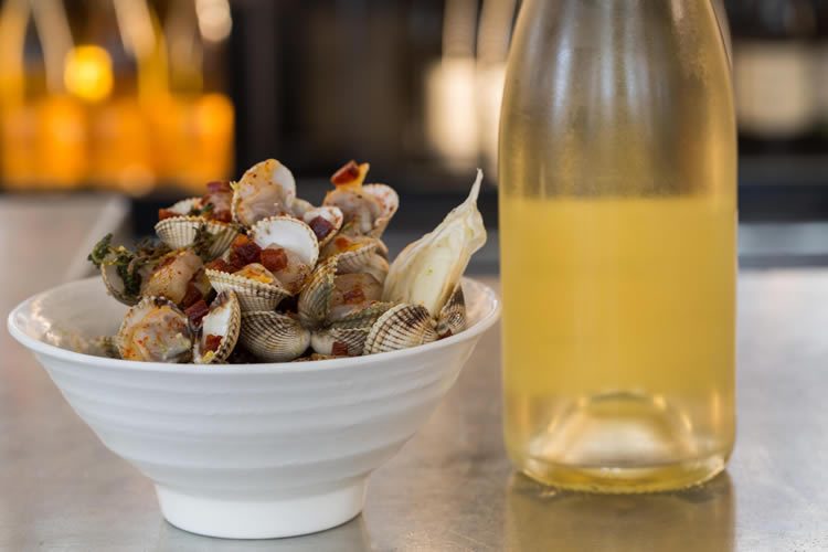 Une assiette de coques et une bouteille de vin blanc sur un comptoir