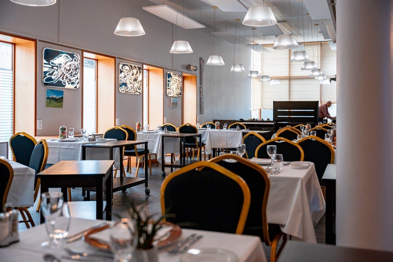 La salle du restaurant Sésame, tables nappées de blanc, chaises noires à dossier doré et suspensions blanches