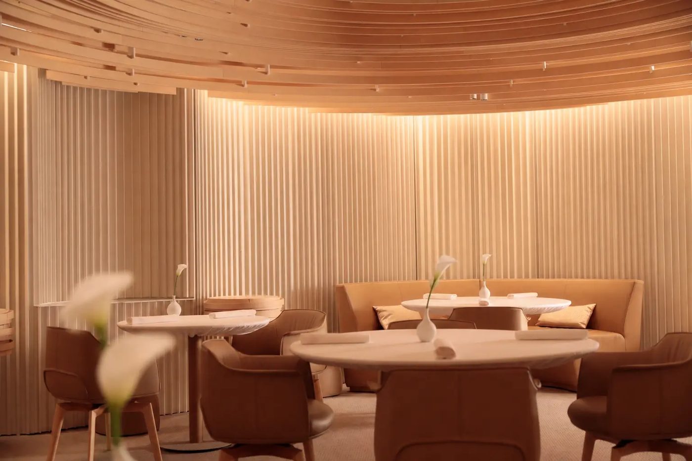 La salle de Blanc sous sa voûte de lattes de bois clair, banquette et fauteuils clairs, arums sur les tables