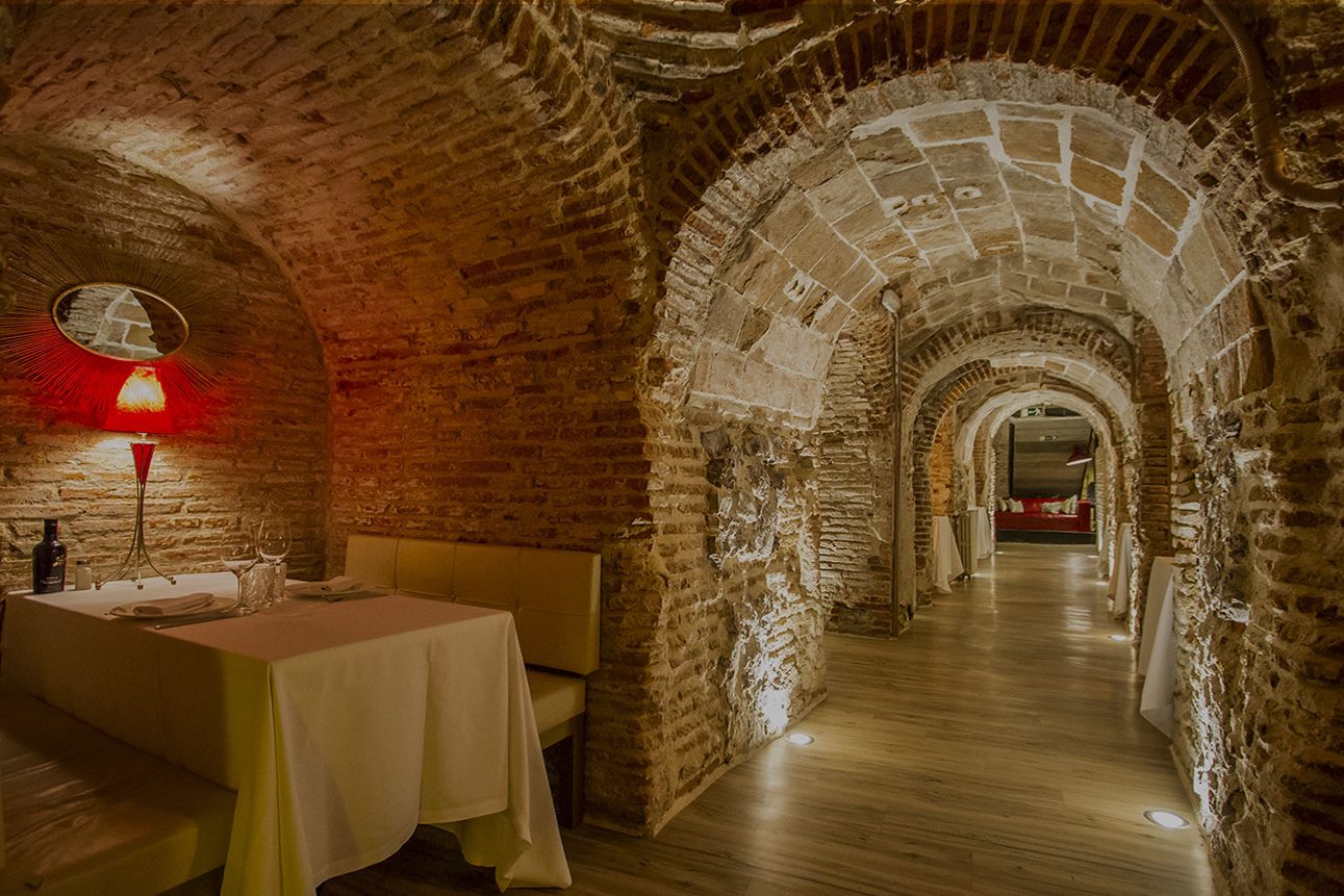 Une alcôve voûtée de briques à la Bodega de los Secretos, table pour deux et couloir de caves éclairé
