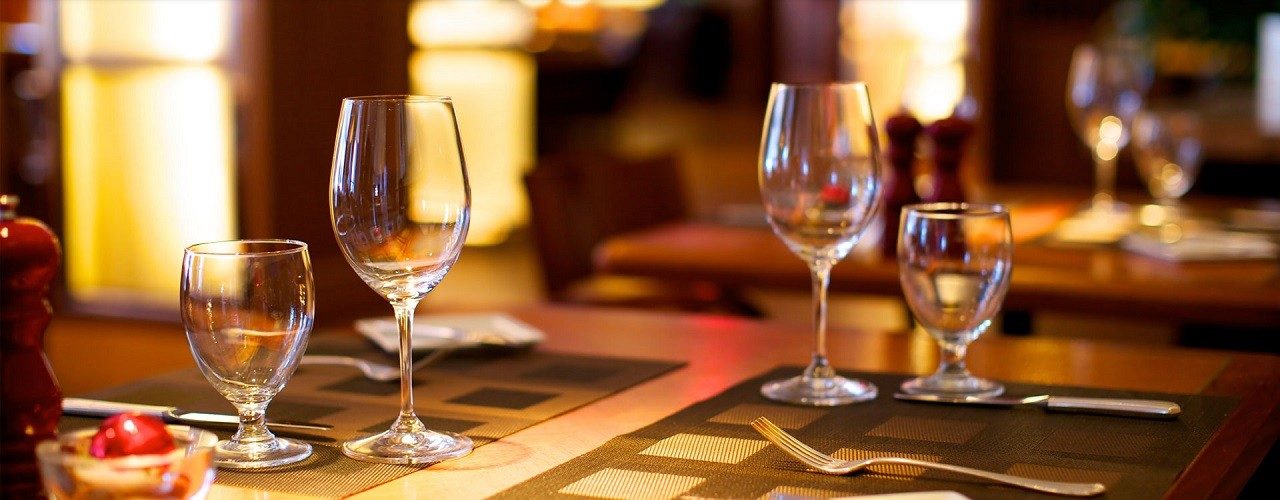 Une table dressée de verres à vin, dans la lumière chaude de la salle de Bong