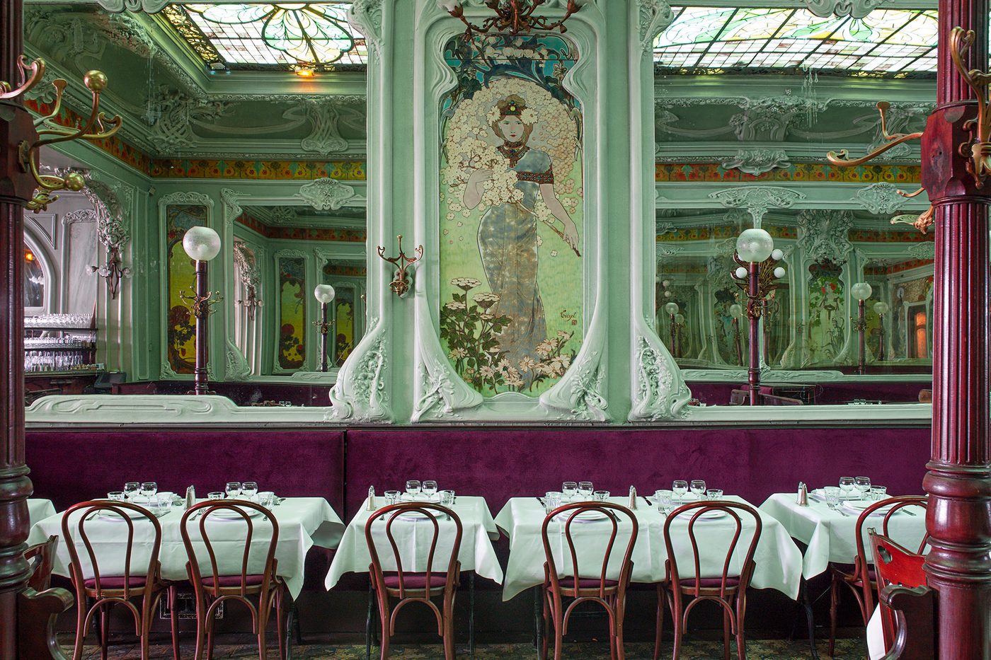 La salle du Bouillon Julien, panneau de verre peint d'une femme-fleur, moulures vert céladon, banquette prune et tables nappées
