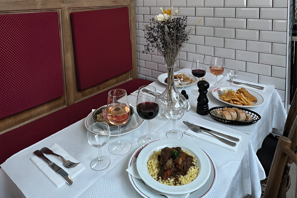 Une table dressée au Bouillon Morny, bœuf bourguignon et frites, verres de vin, banquette rouge et carreaux blancs