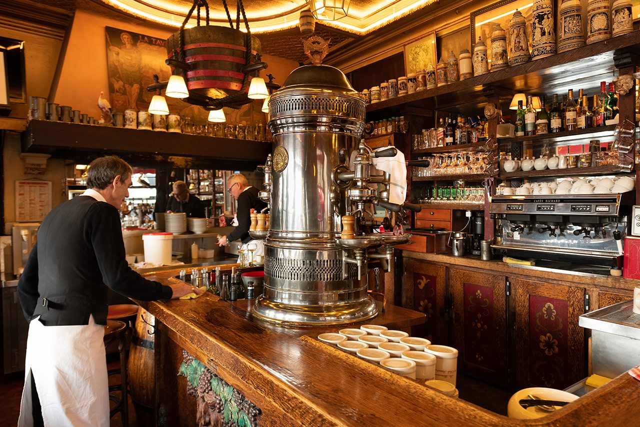 Le comptoir de bois de la Brasserie de l'Isle Saint-Louis, sa colonne à bière chromée et un serveur en tablier blanc