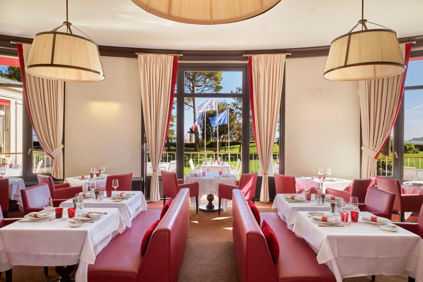 La salle de La Brasserie du Royal, banquettes rouges, tables nappées de blanc, suspensions et rideaux ouverts sur le jardin