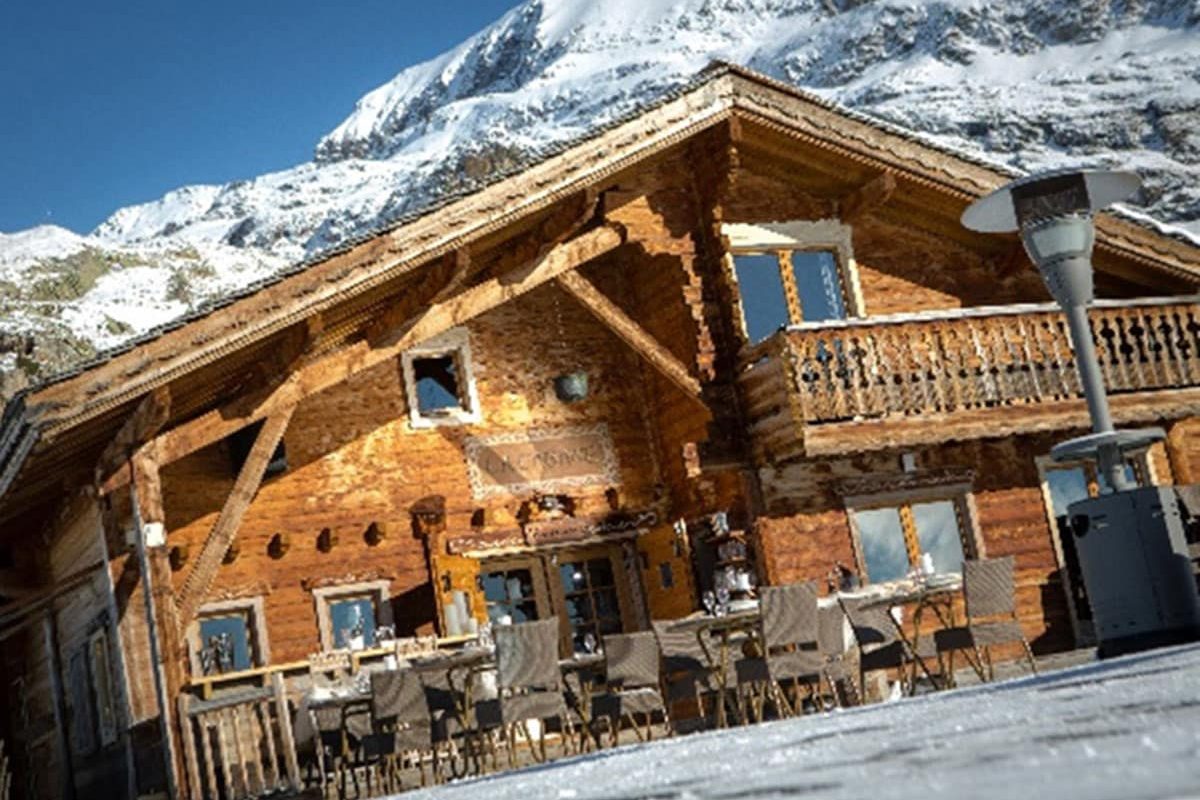 Le chalet de bois de La Cabane, son balcon et sa terrasse au soleil, sommet enneigé derrière