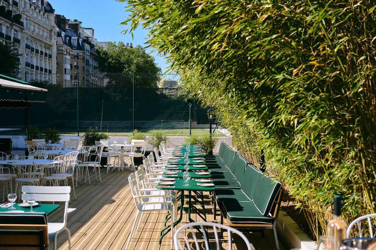 La terrasse du Café Court, banquette et tables vertes le long d'une haie de bambous, court de tennis au fond