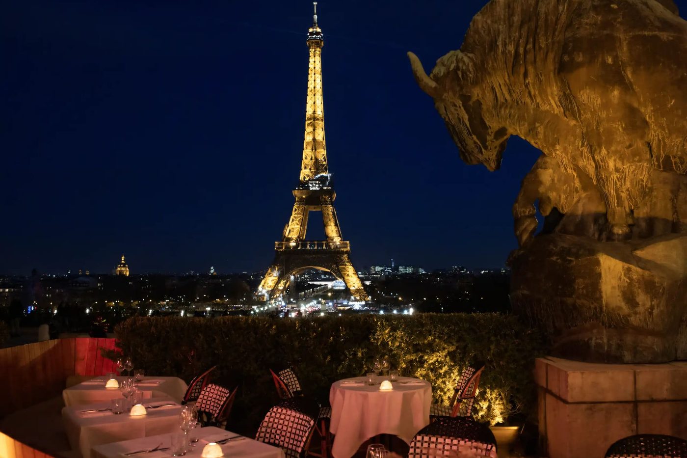 La terrasse du Café de l'Homme la nuit, tables nappées et photophores, la tour Eiffel illuminée au fond