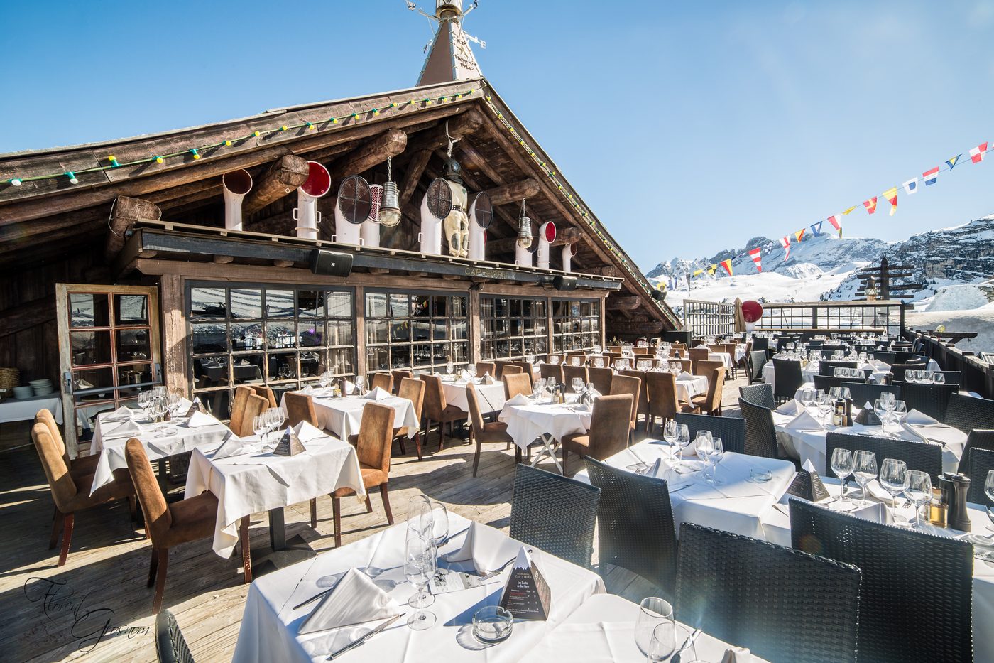 La terrasse du Cap Horn sous le soleil, tables nappées de blanc devant le chalet et les pistes enneigées