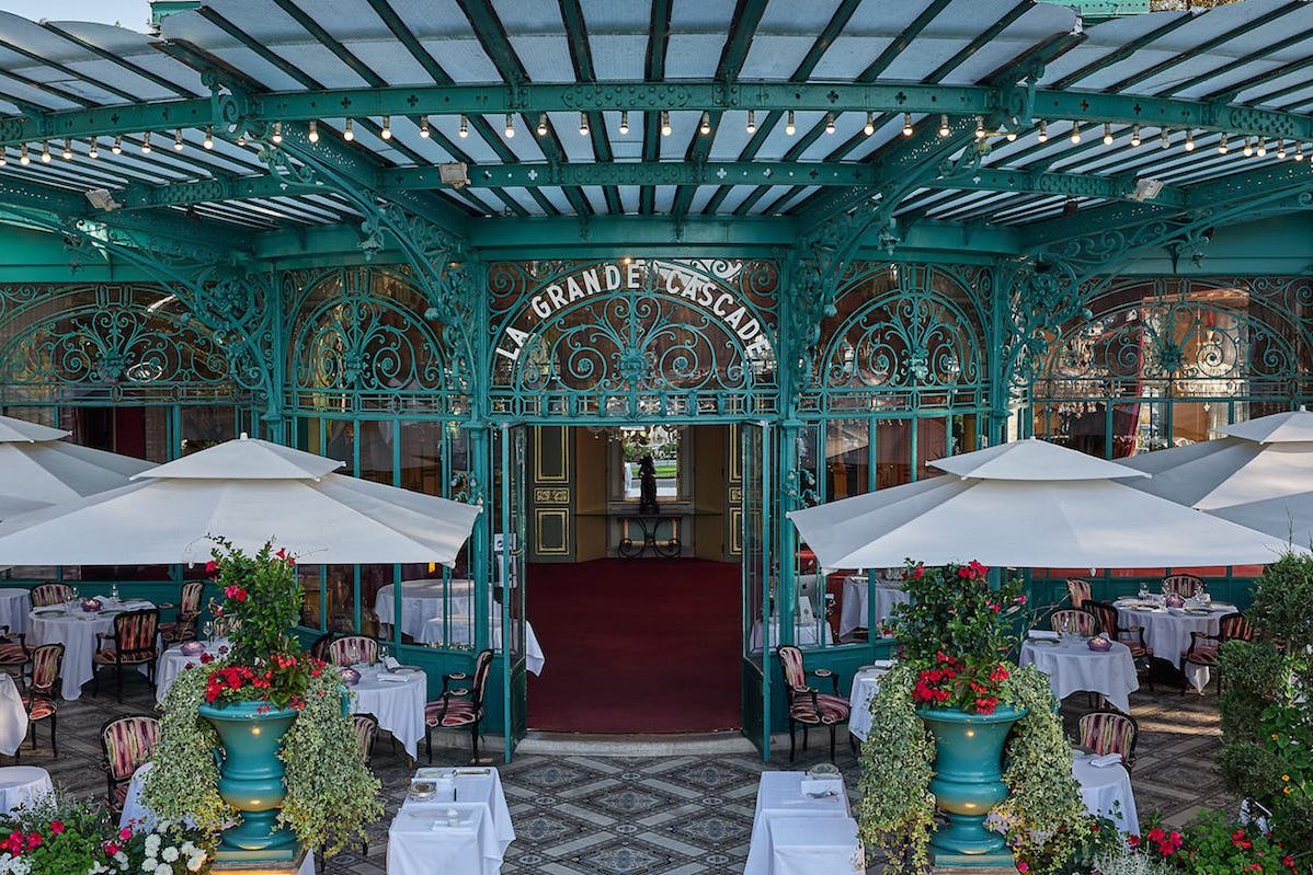 La terrasse de La Grande Cascade sous la marquise de verre et de métal vert, parasols blancs et tables nappées