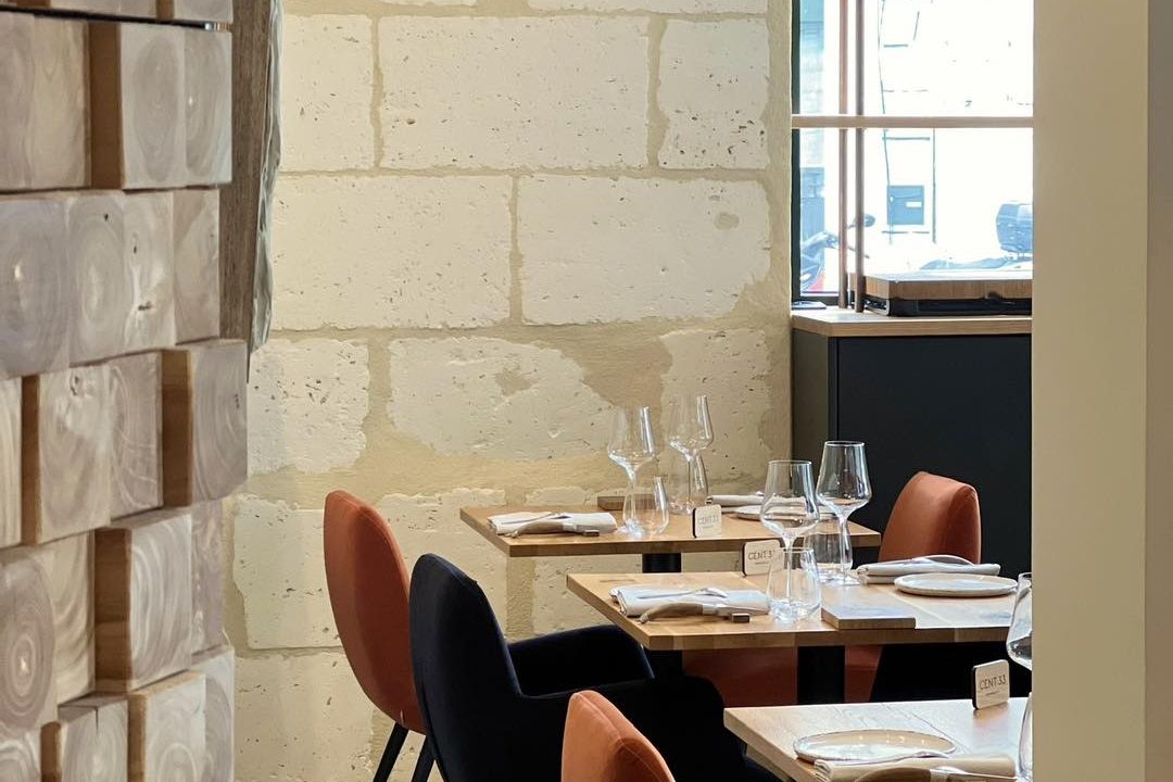 La salle de Cent33 : mur de pierre blonde, tables en bois dressées et chaises en velours rouille et bleu nuit