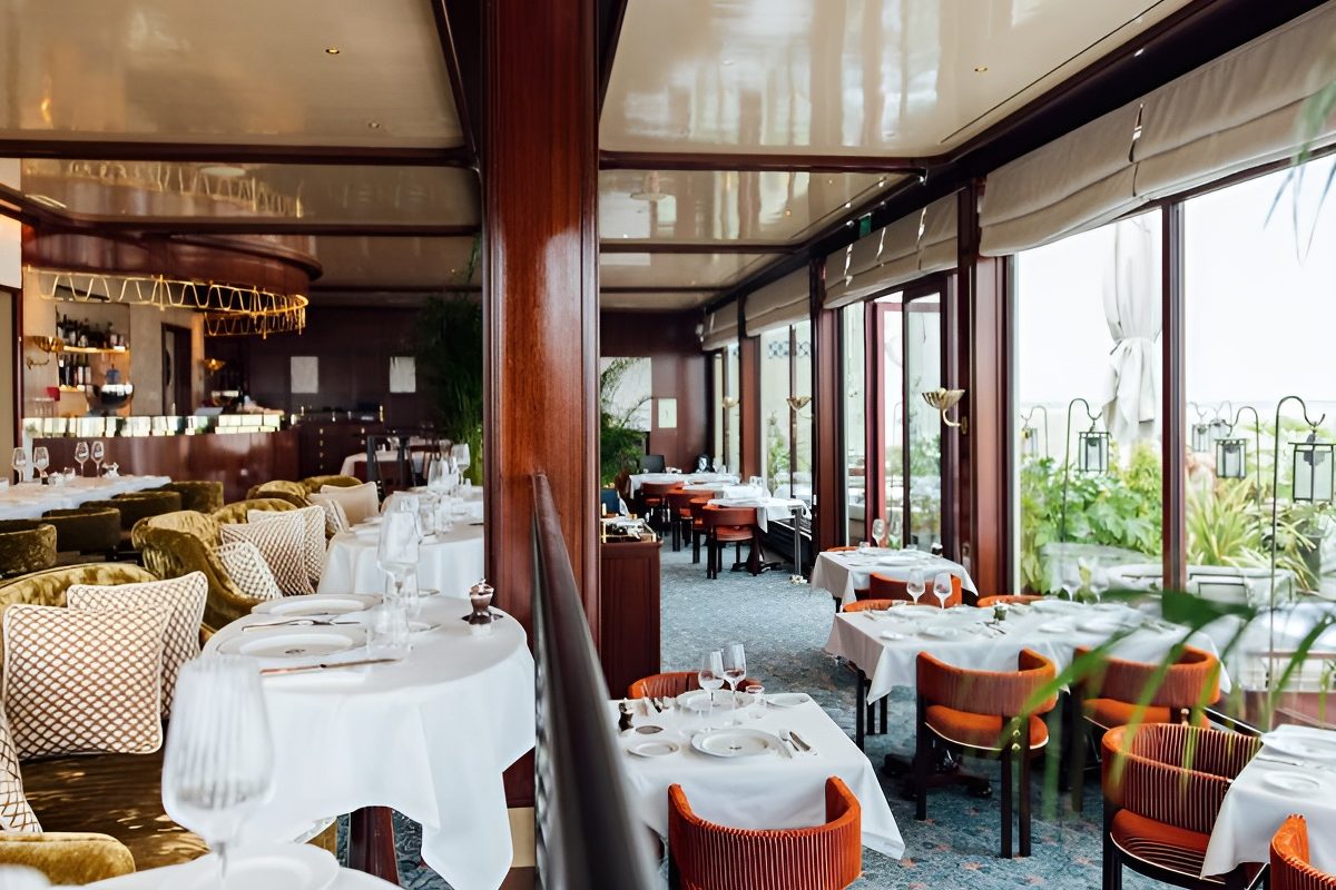La salle du Ciro's, tables nappées de blanc, fauteuils de velours et grandes baies ouvertes sur la mer
