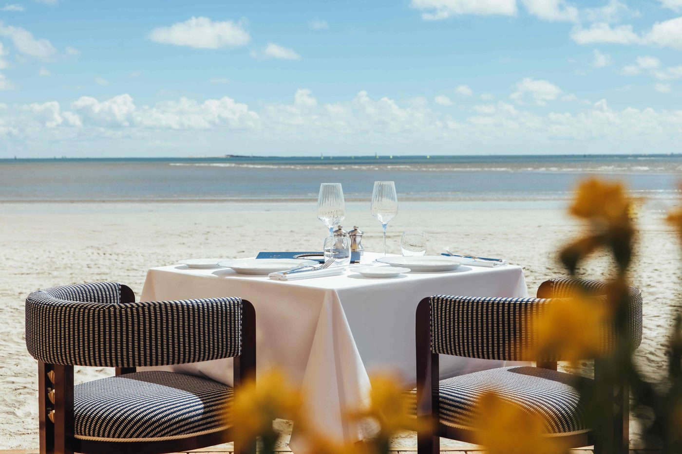 Une table dressée sur le sable devant le Ciro's, fauteuils rayés, la plage et la baie de La Baule derrière