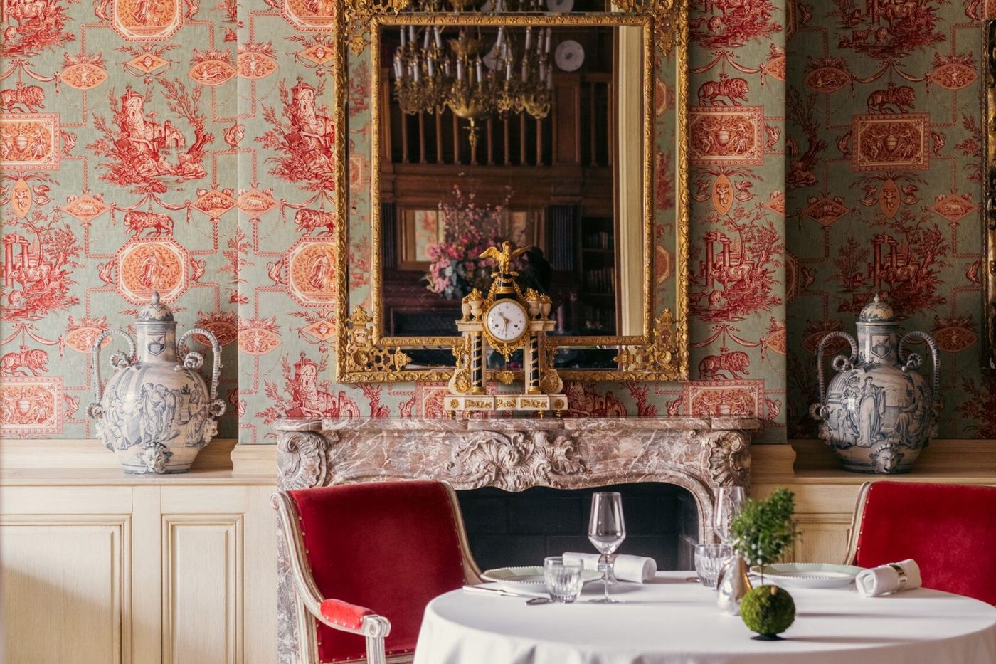 La salle à manger Lestonnac du Clarence : murs tendus de tissu imprimé rouge, cheminée de marbre, miroir doré, table ronde et fauteuils rouges