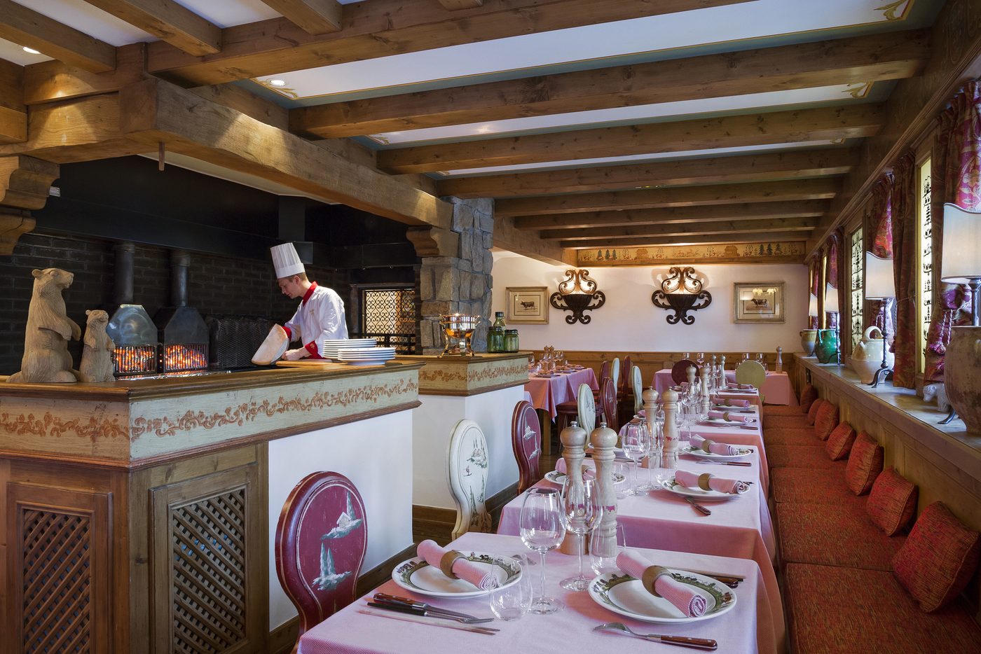 La salle du Coin Savoyard, poutres, nappes roses et cuisinier devant le four au fond de la salle