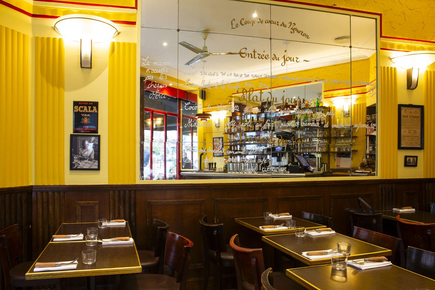 La salle du Comptoir du Relais, murs jaunes, lambris sombres et grand miroir où sont peints les plats du jour