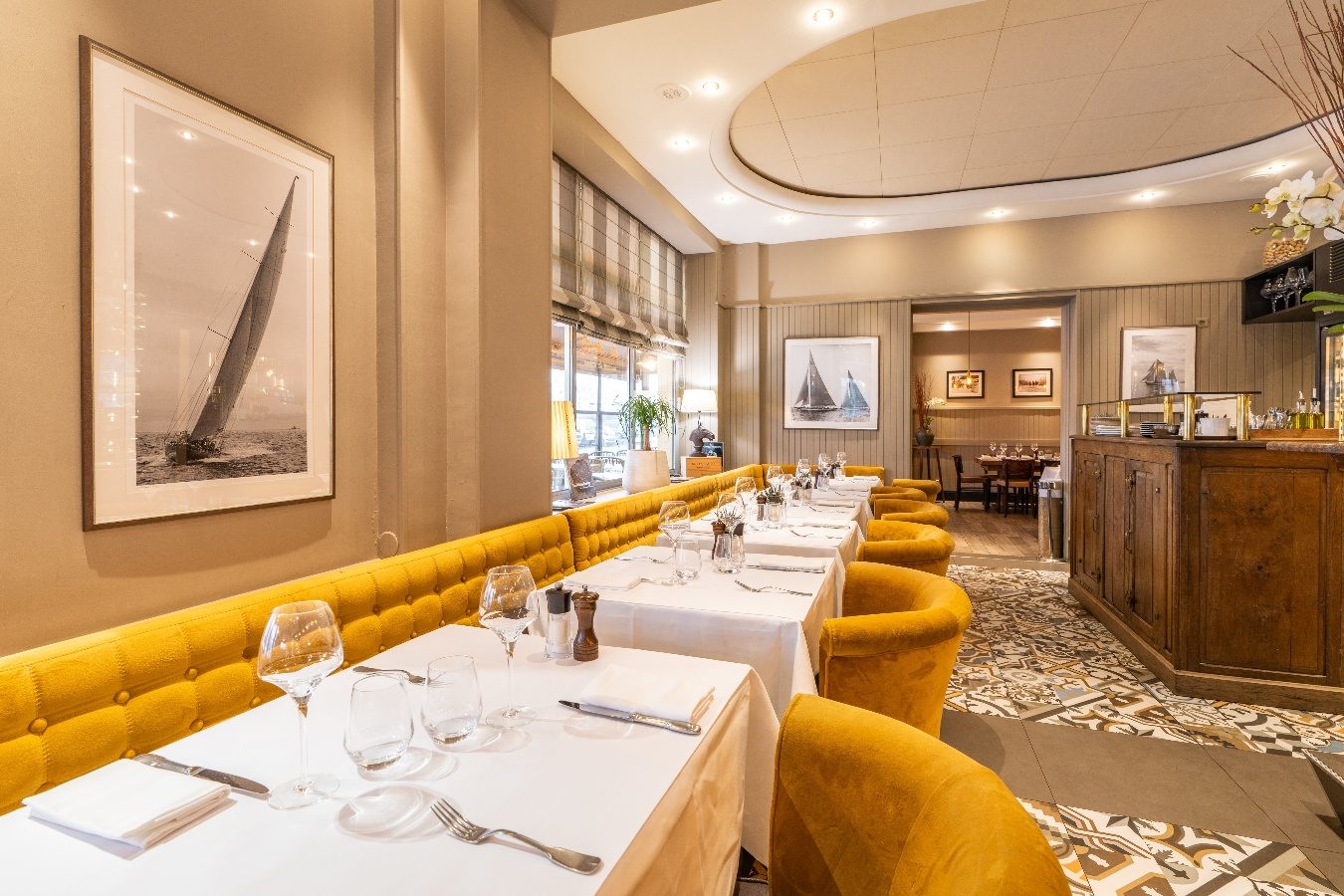 La salle du Comptoir et la Table, banquette jaune, tables nappées de blanc et photographie de voilier