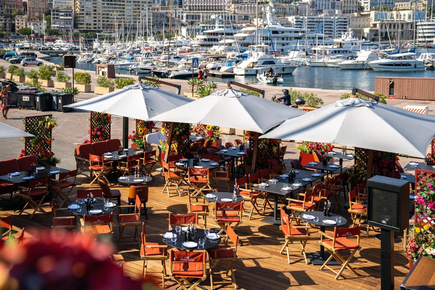 La terrasse de Crazy Pizza sous ses parasols blancs, avec les yachts du port Hercule en arrière-plan