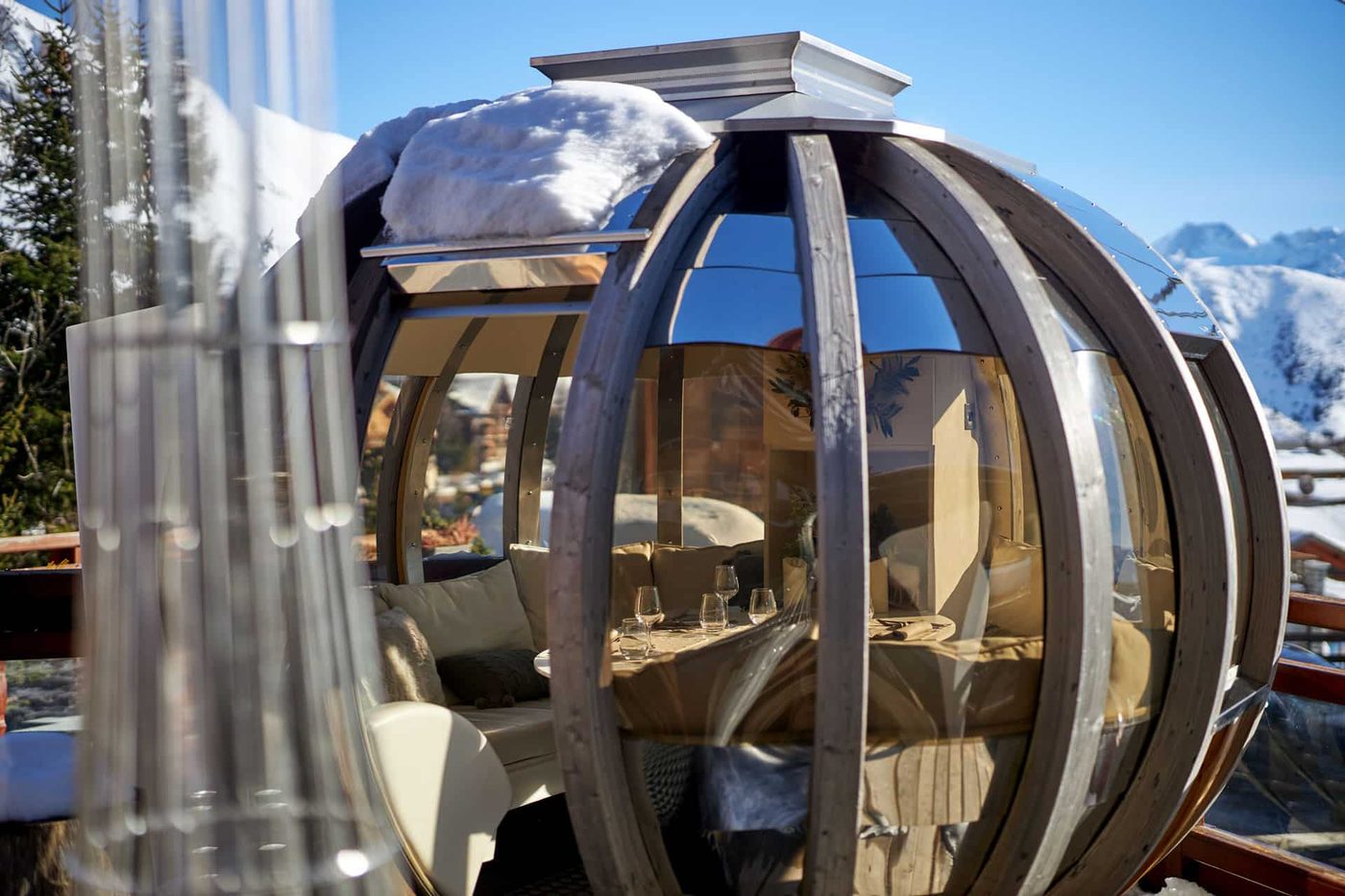 Une bulle de verre et de bois sur la terrasse de L'Espérance, table dressée à l'intérieur, neige sur le toit