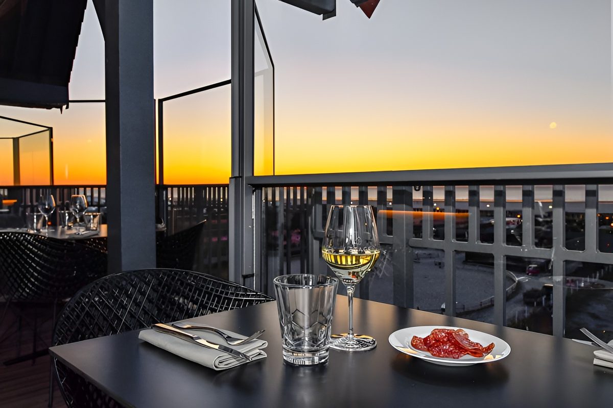 Une table dressée sur la terrasse de L'Étage au coucher du soleil, ciel orangé au-dessus de la mer