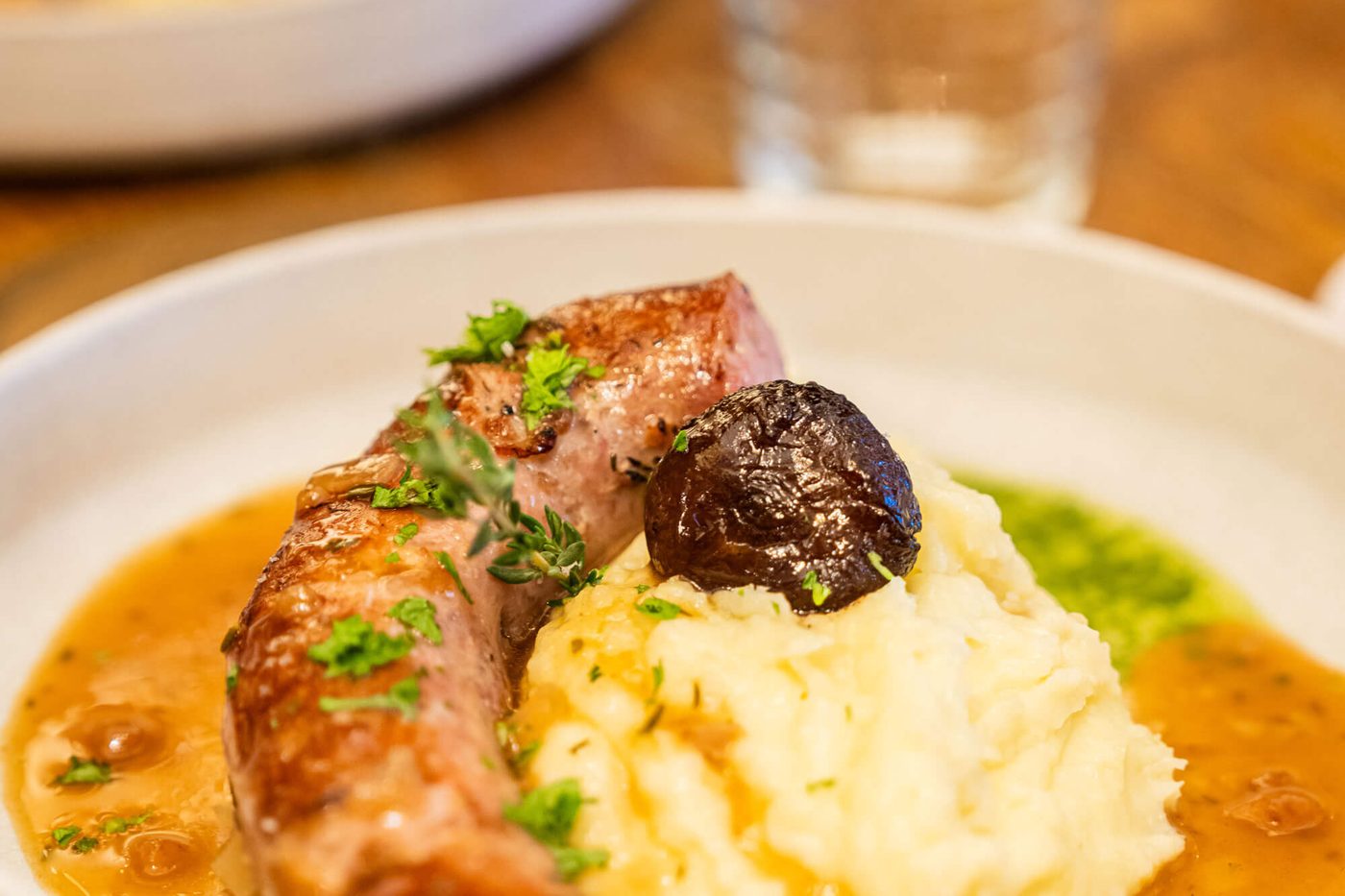 La saucisse de montagne et sa purée maison, nappées de jus, dans une assiette creuse des Fous de l'Île