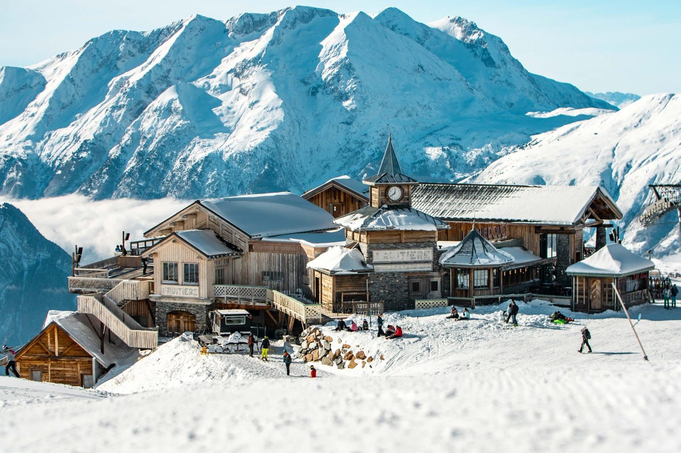 Les chalets de bois de La Folie Douce sur la neige, au pied de sommets enneigés, skieurs sur la piste
