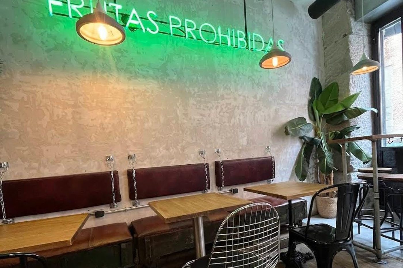 La salle de Frutas Prohibidas : enseigne néon verte sur un mur de pierre, banquettes bordeaux et tables en bois