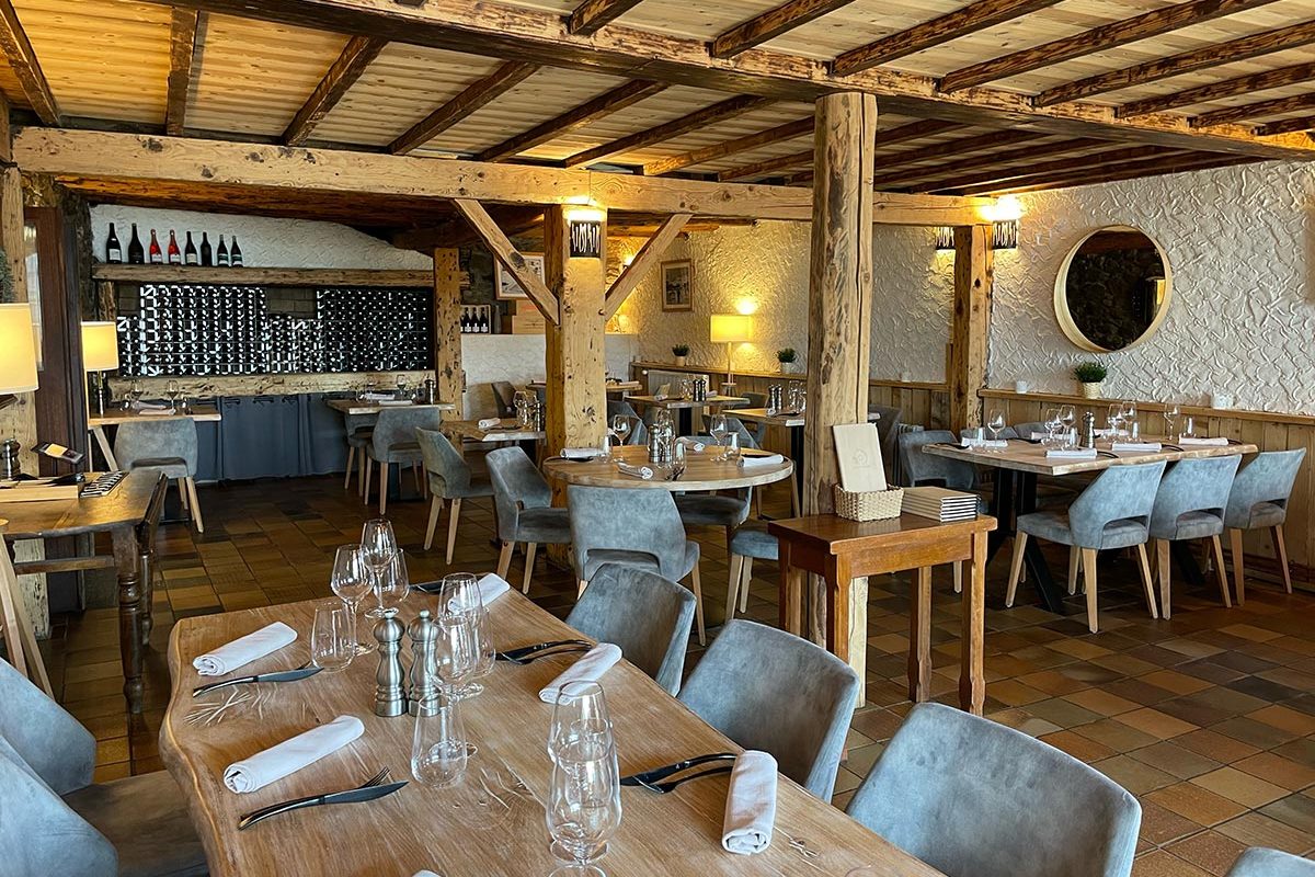 La salle du Génépi, poutres de bois clair, tables dressées et fauteuils gris, bouteilles alignées au fond
