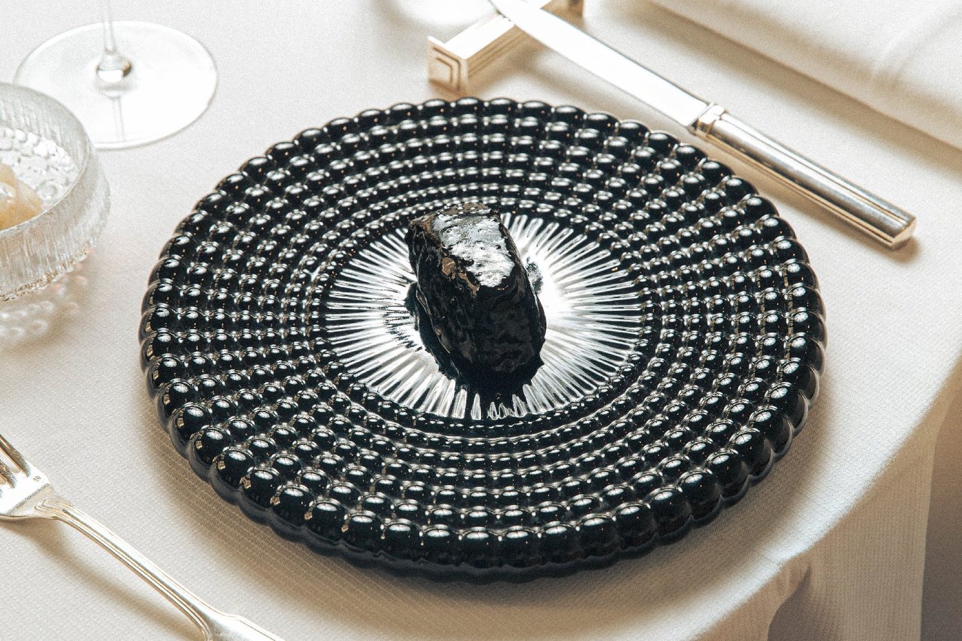 Une assiette de verre noir dressée chez Geoélia, sur une nappe blanche