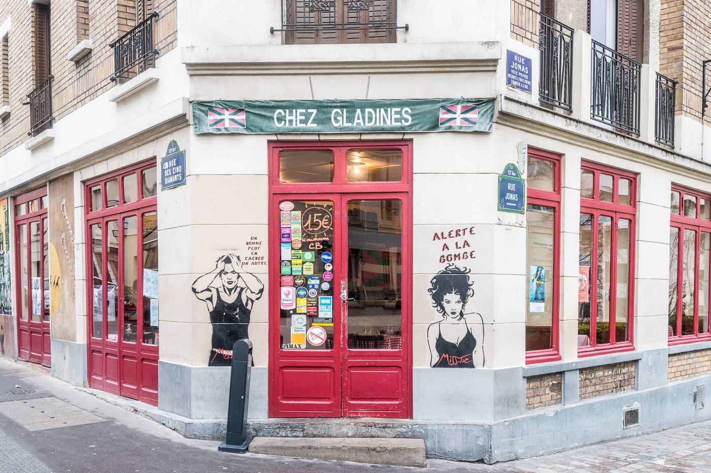 La façade d'angle de Chez Gladines, menuiseries rouges, bandeau vert et drapeaux basques