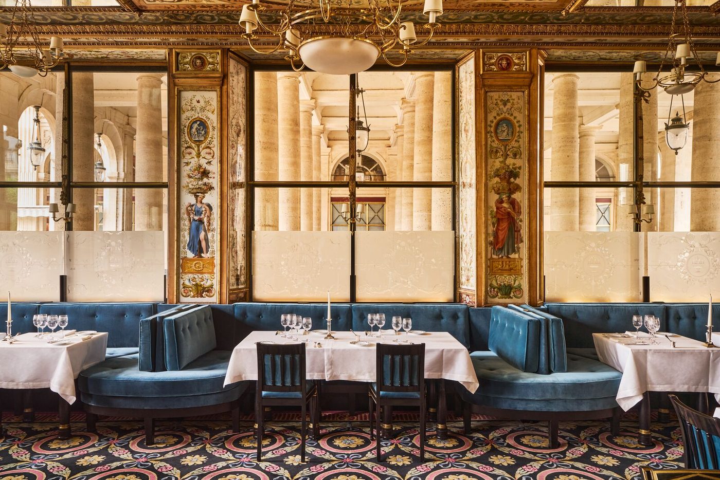 La salle du Grand Véfour : banquettes de velours bleu, tables nappées de blanc, miroirs et peintures sous verre