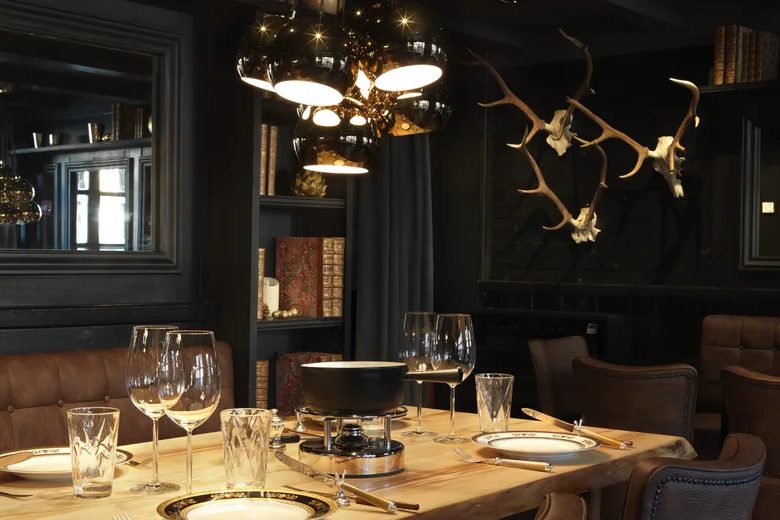 La salle sombre des Grands Crus de Fondues, trophées de bois au mur, suspensions dorées et table dressée