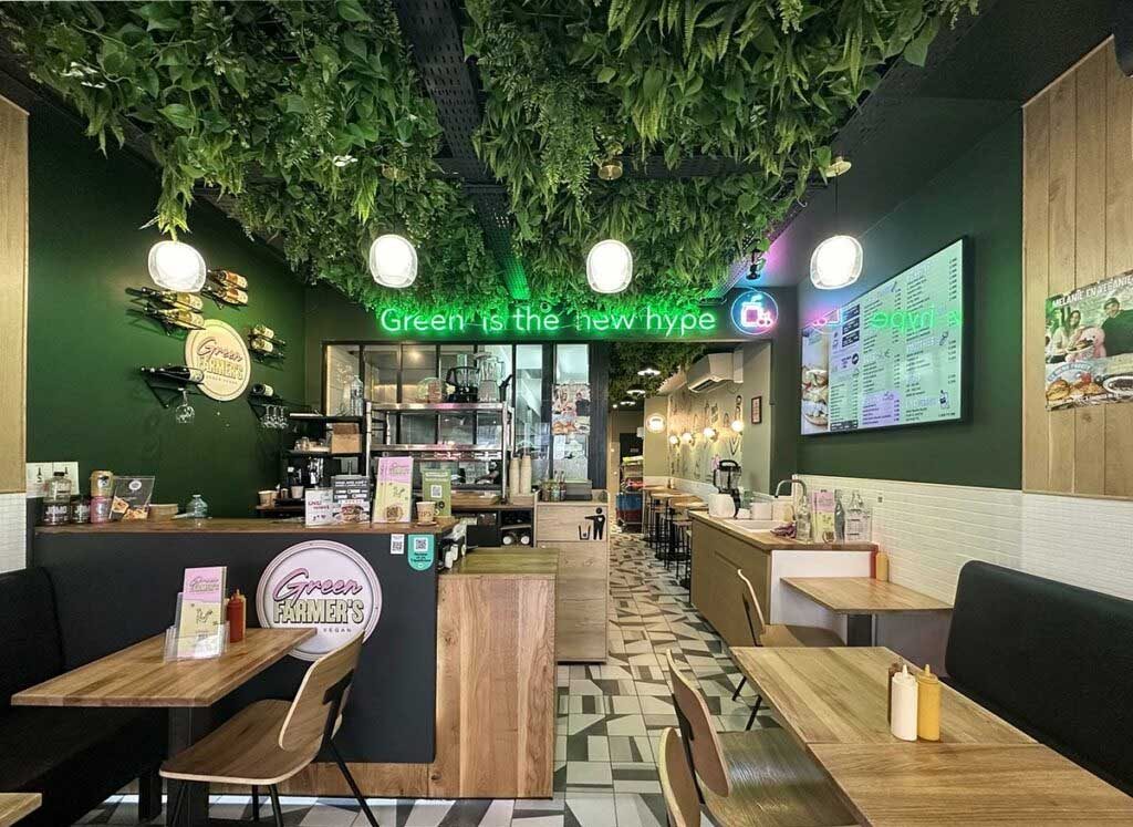 La salle d'un restaurant Green Farmer's, plafond végétalisé, néons, banquettes noires et tables en bois