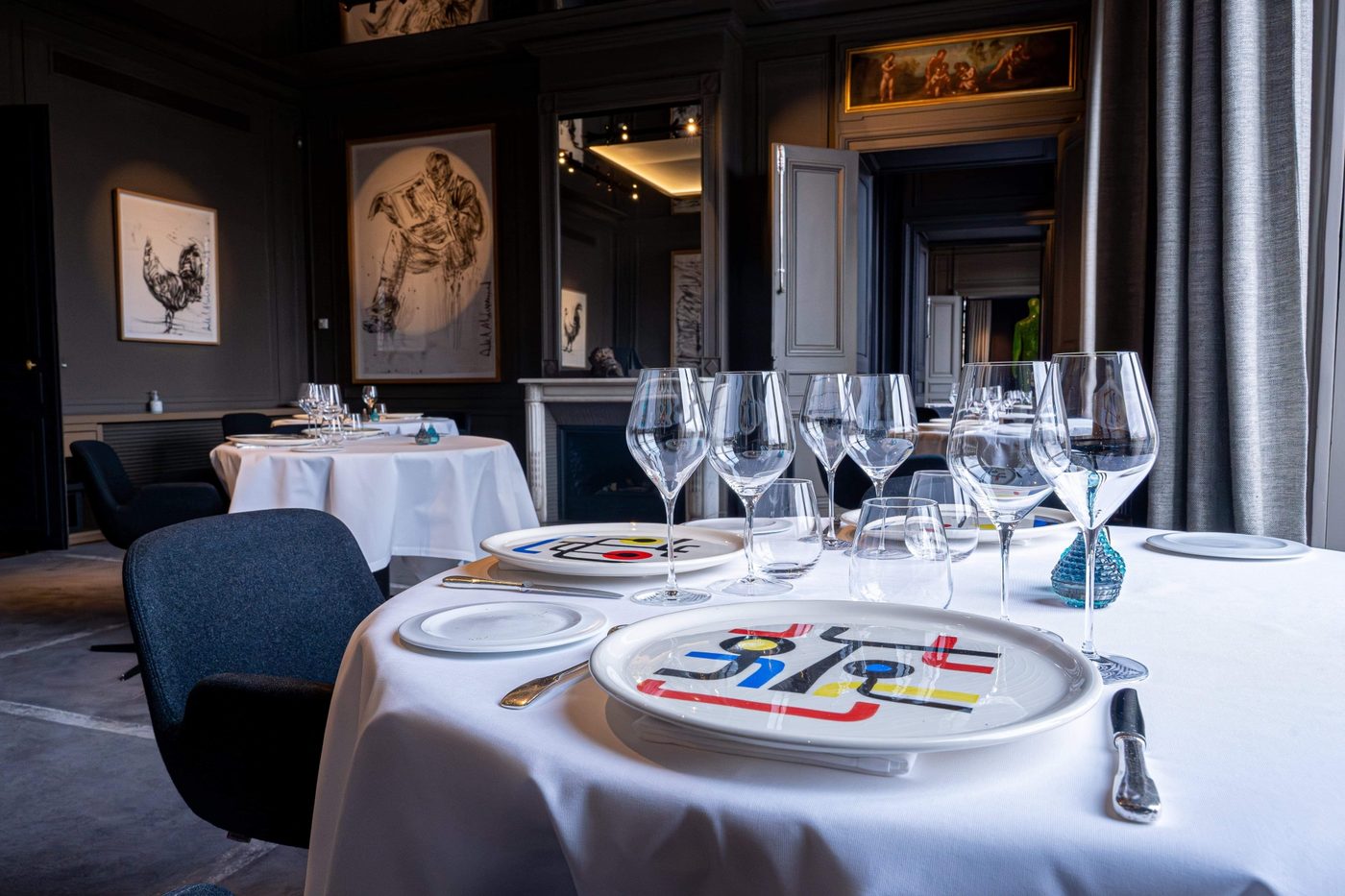 Le salon Vert Galant du restaurant Guy Savoy : table ronde nappée de blanc, verres dressés, murs gris sombre et cheminée à miroir