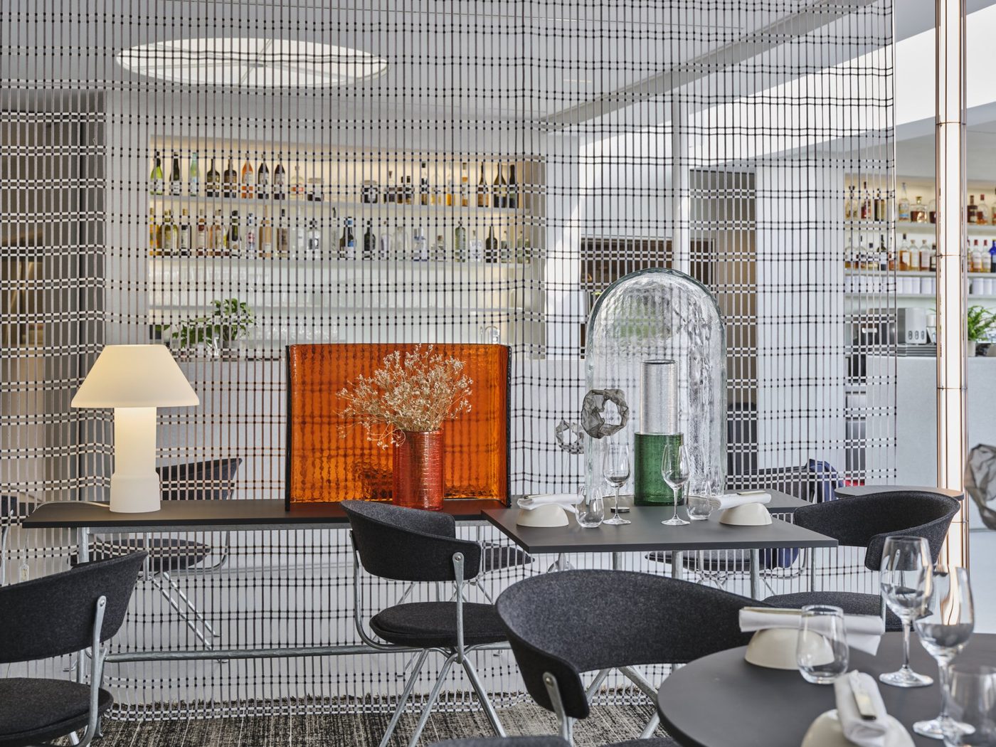 La salle de la Halle aux Grains, tables sombres et chaises noires devant un bar aux étagères lumineuses
