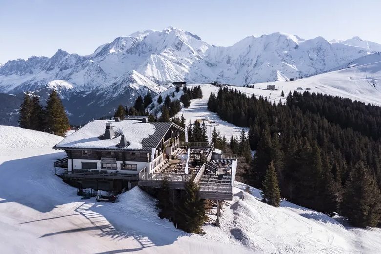 Le chalet de l'Idéal 1850 sur la neige, entouré de sapins, avec le massif du Mont-Blanc en arrière-plan
