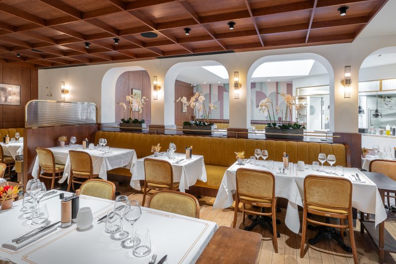 La salle de L'Institution, banquettes moutarde, tables nappées, arcades blanches et verrière