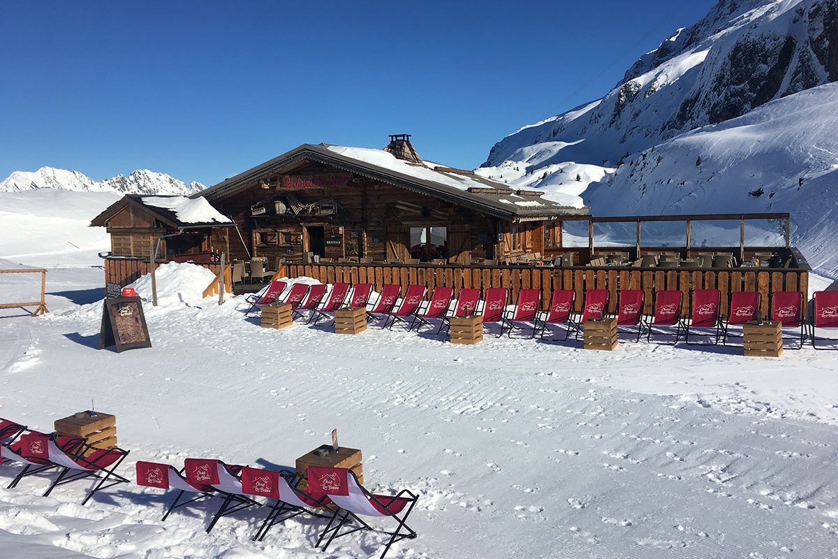 Le Chalet du Lac Besson dans la neige, transats rouges alignés devant la terrasse, montagne en arrière-plan