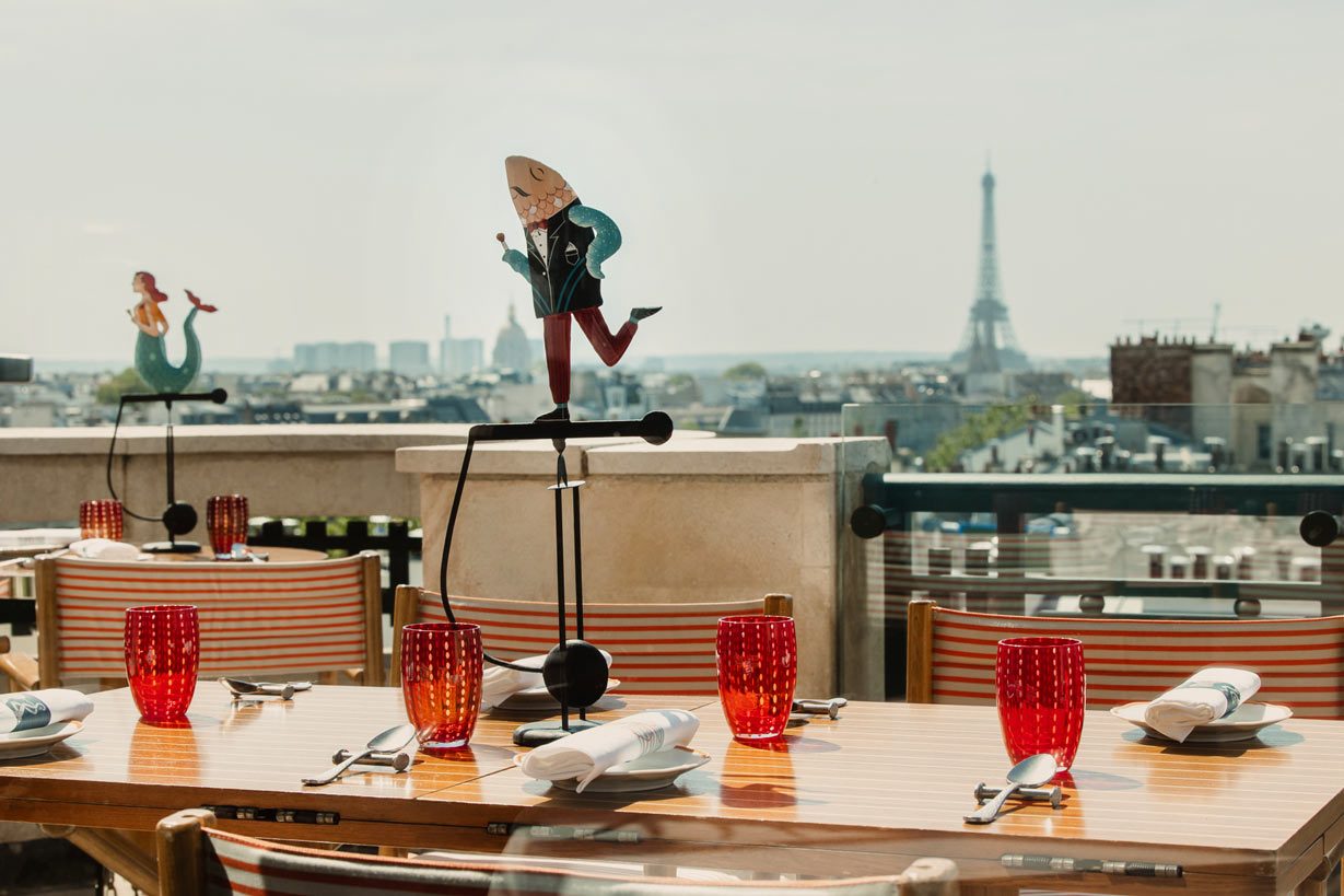 Une table dressée de verres rouges chez Langosteria, avec les toits de Paris et la tour Eiffel à l'horizon