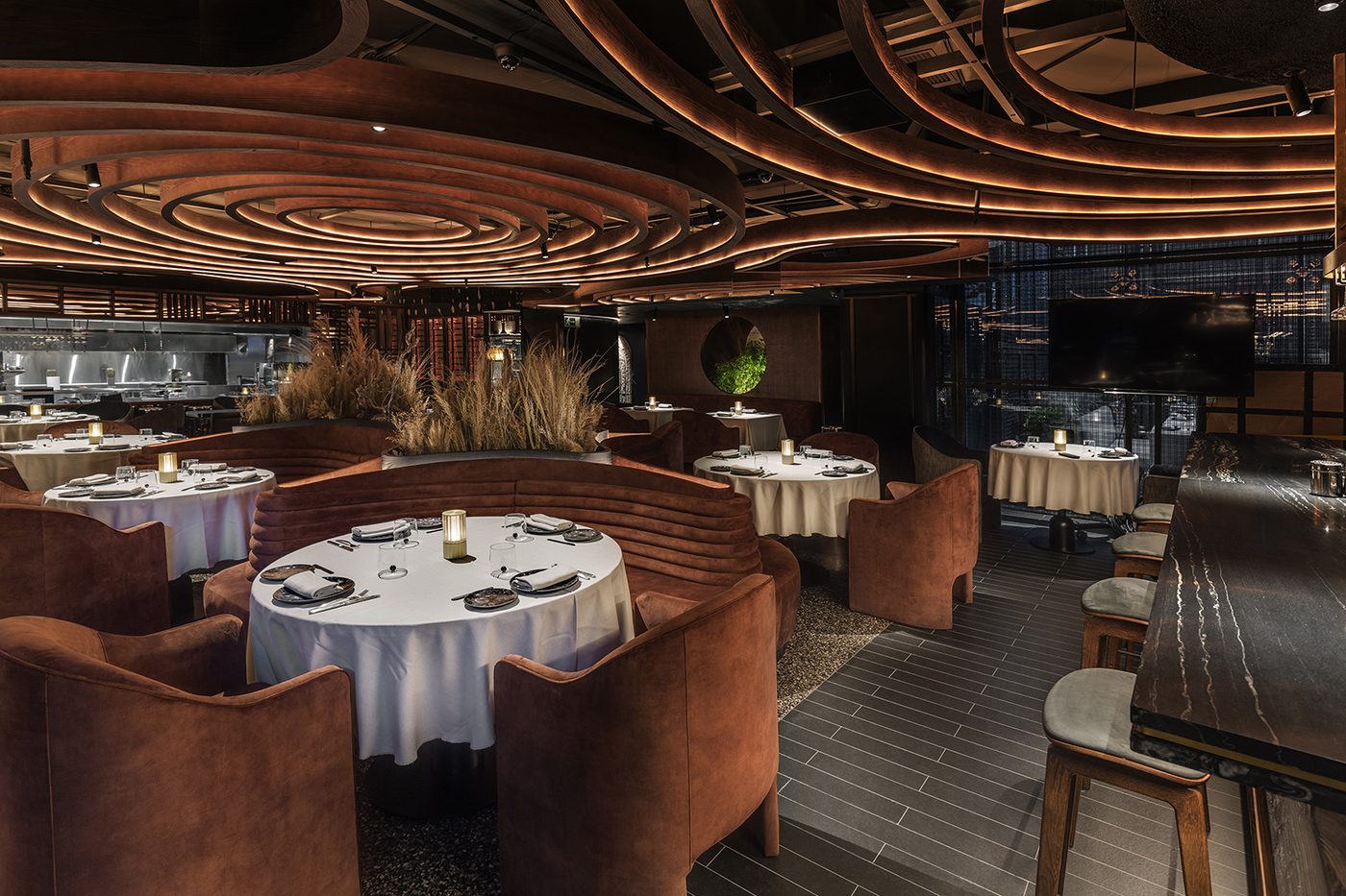 La salle de Leña Madrid : plafond de lattes de bois courbes éclairées, fauteuils en velours brique
