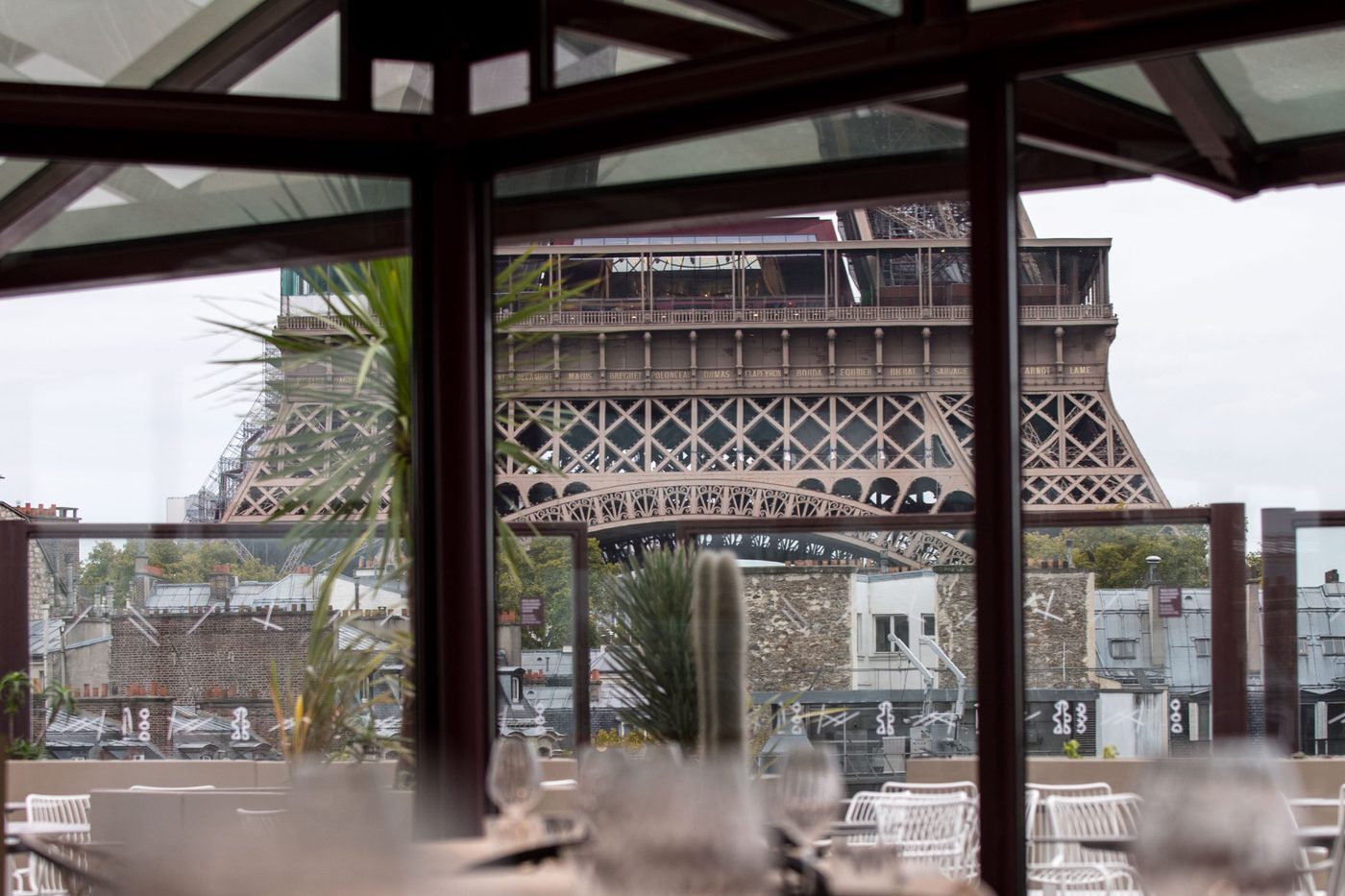 Vue à travers la verrière des Ombres : le premier étage de la tour Eiffel au-dessus d'une rangée de toits