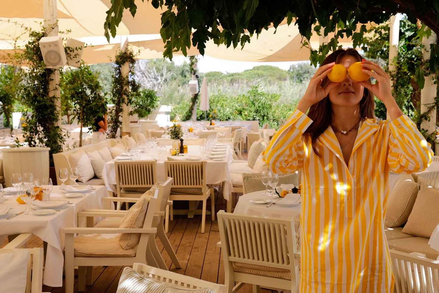 La terrasse de Loulou à Ramatuelle, tables nappées sous les pins et une convive en robe rayée jaune