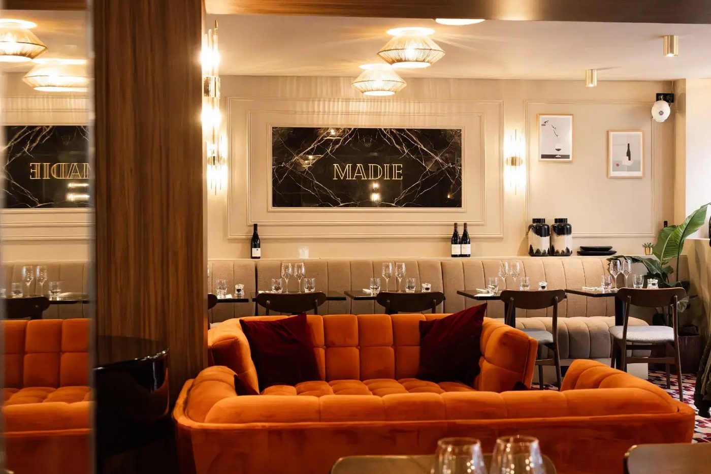 La salle de Madie, canapé capitonné en velours orange, banquette beige et panneau de marbre noir marqué Madie